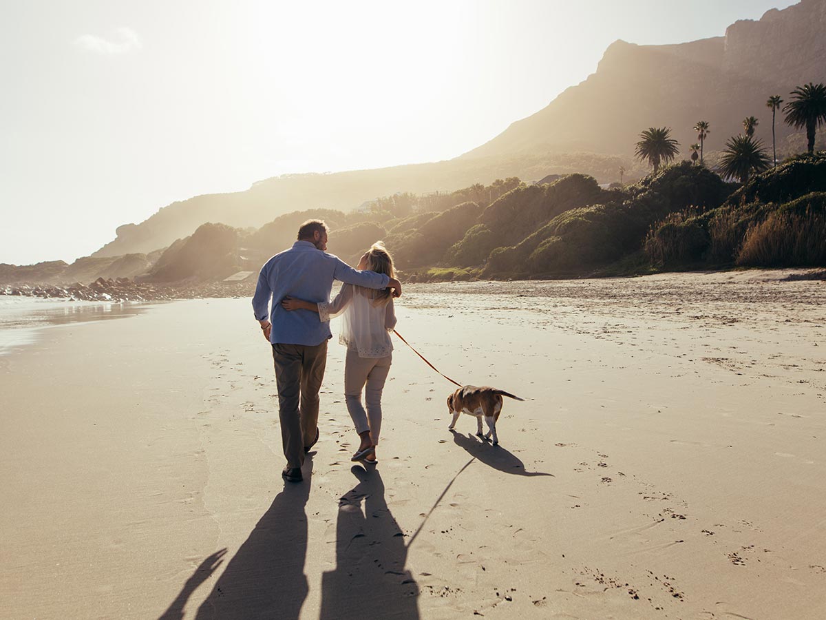 retired couple walking on beach with their dog