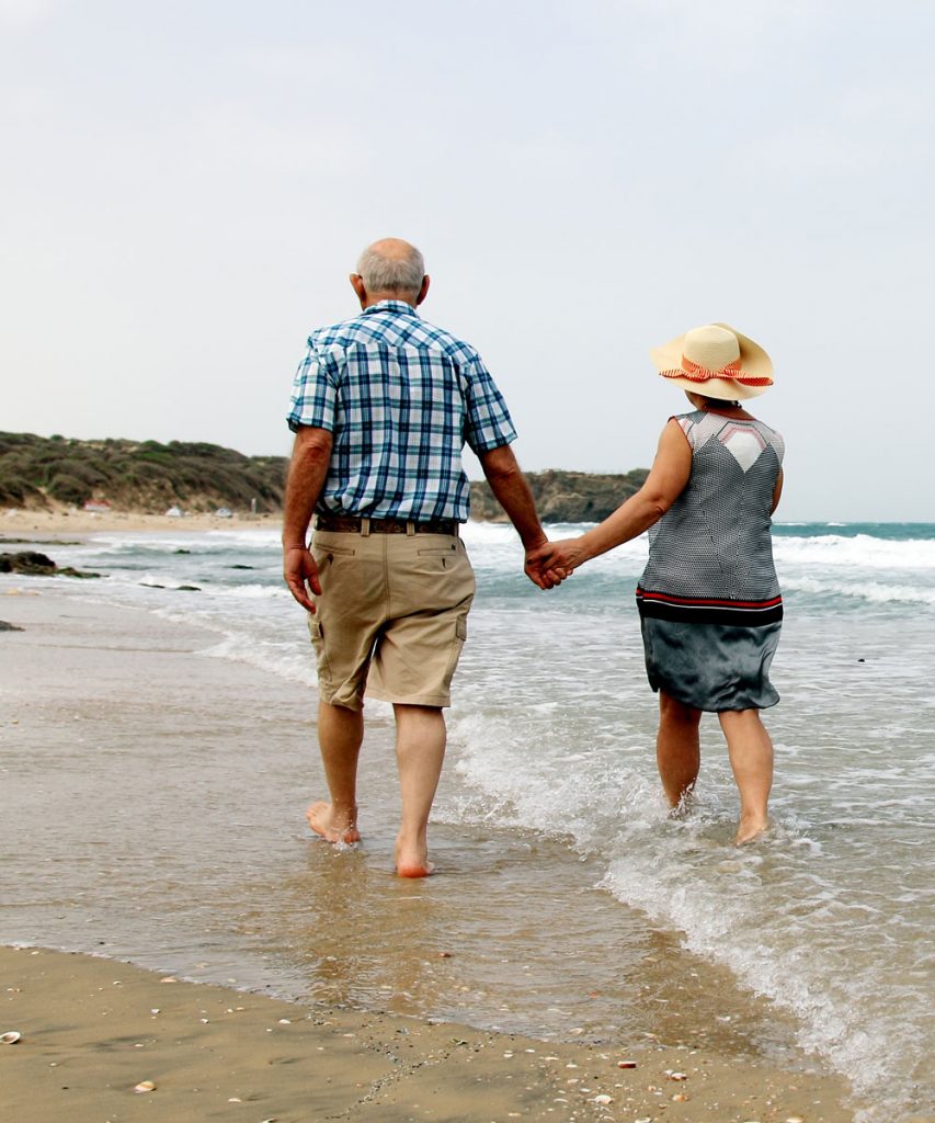 Retired couple walking along beach holding hands